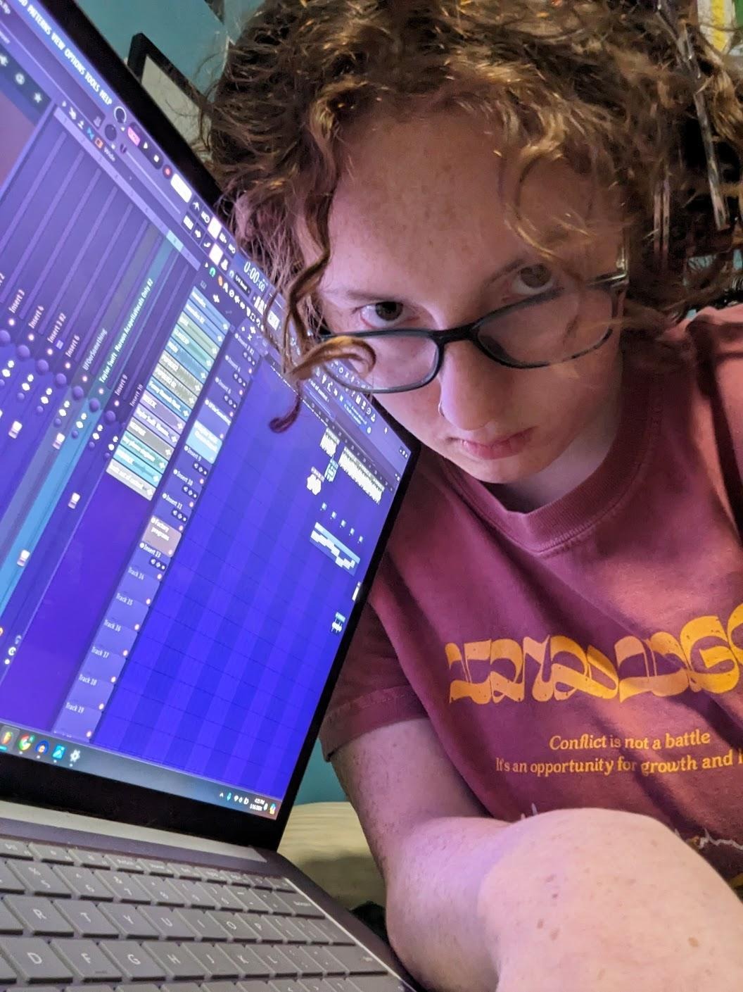 they/them grandson looks intensely at the camera next to their computer, which is open to FL studio