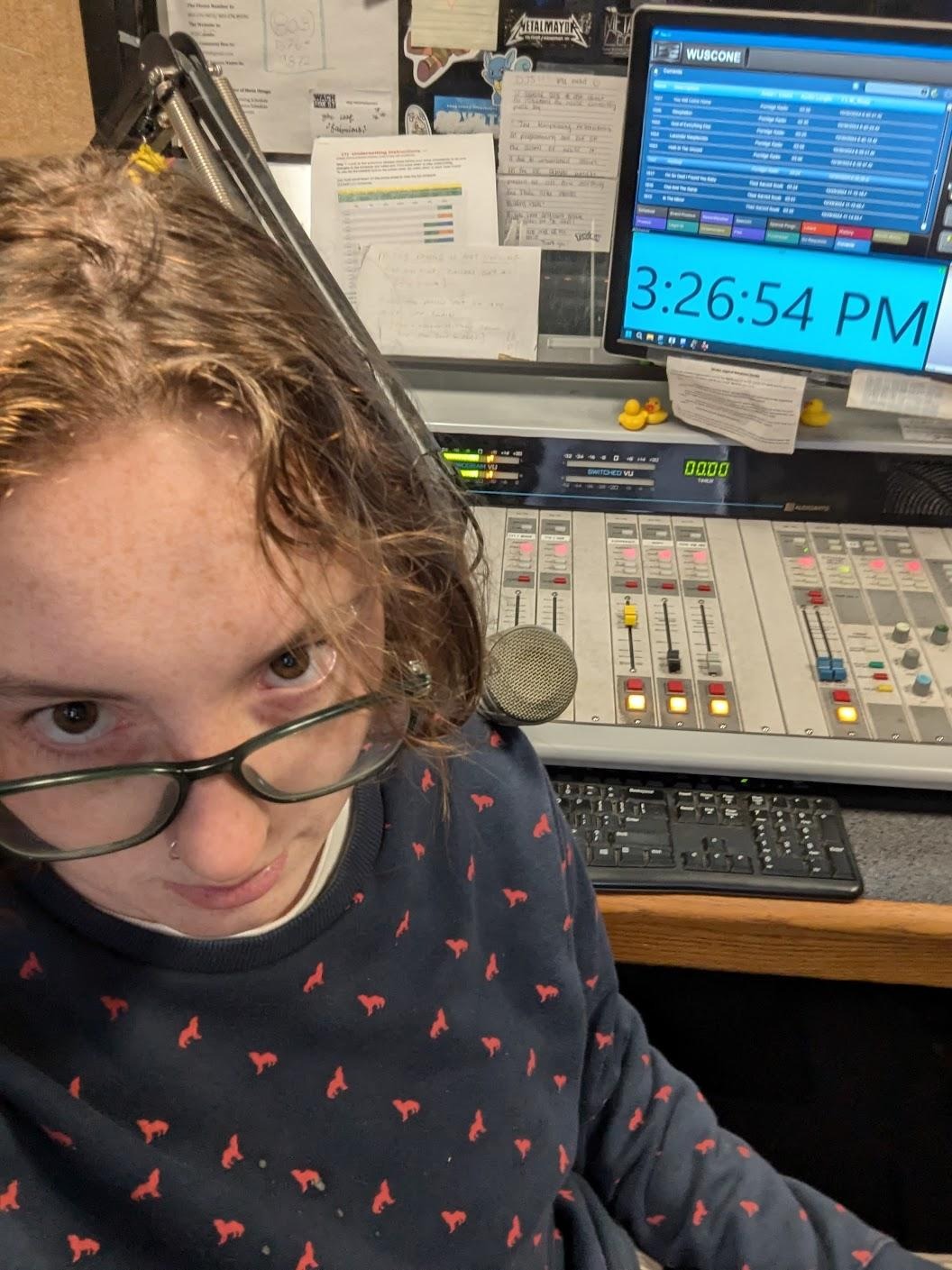 they/them grandson sits in a radio station. the time on the clock reads 3:26:54