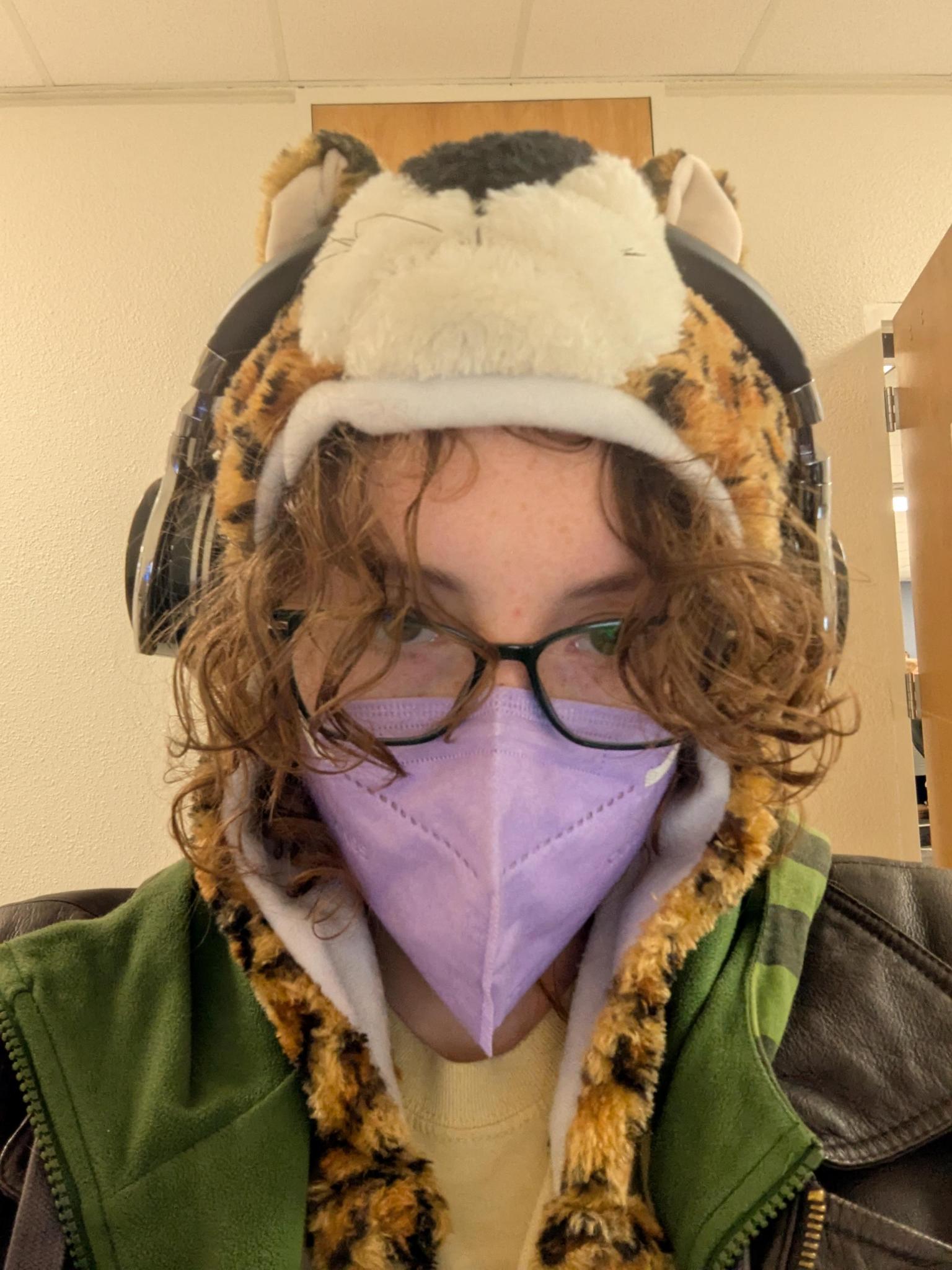 they/them grandson wearing a purple mask, glasses and a tiger hat.